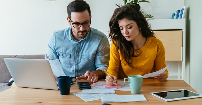 Couple sitting at a kitchen table reviewing bills and budget, looking concerned about rising homeownership costs and monthly housing expenses